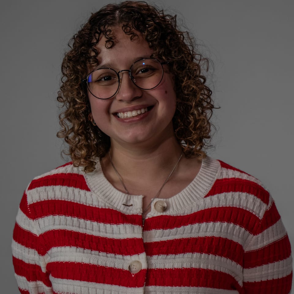 Smiling woman with curly hair and round glasses in a red-and-white striped cardigan.