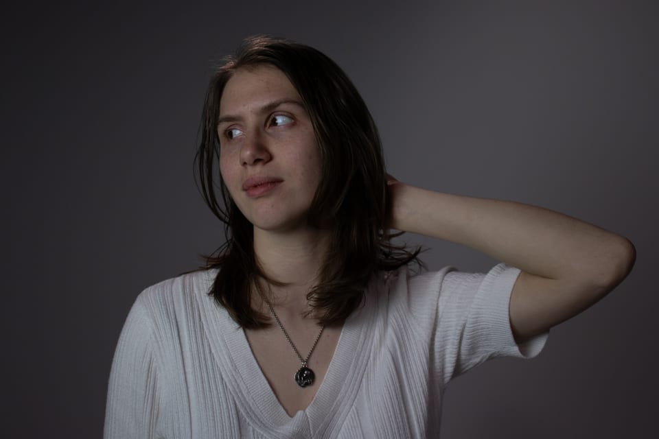 Woman glancing over her shoulder with one hand in her hair, against a dark backdrop.