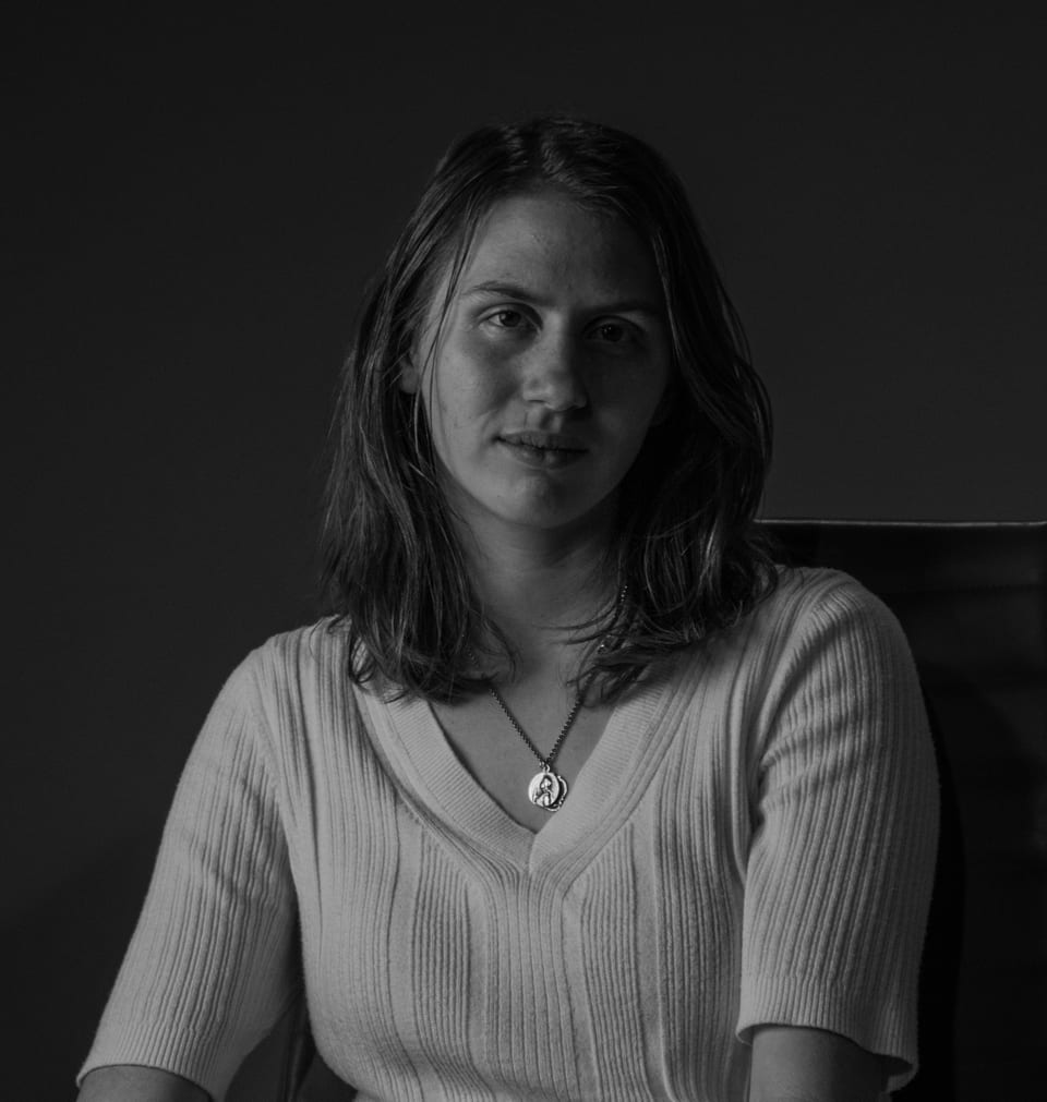 Black-and-white portrait of a woman seated in a chair, a pendant at her collar.