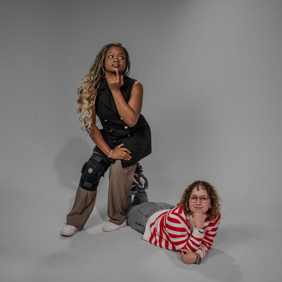 Two friends posing: one leaning on her knee in a thinking pose, the other lying on the floor behind her, chin in hand.