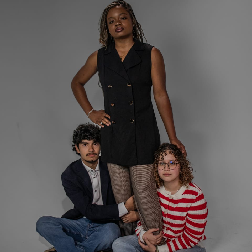 Three friends posed together: one standing with a hand on her hip, two seated at her feet.