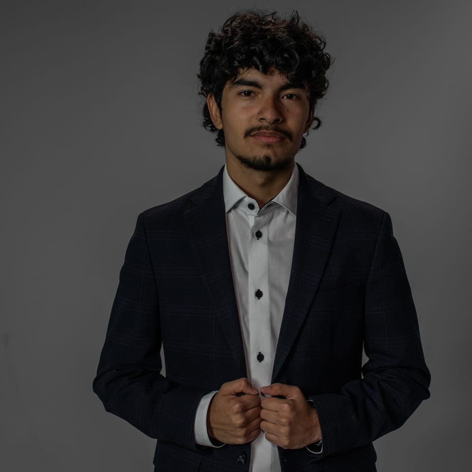 Young man in a dark blazer buttoning his jacket, looking straight into the camera.