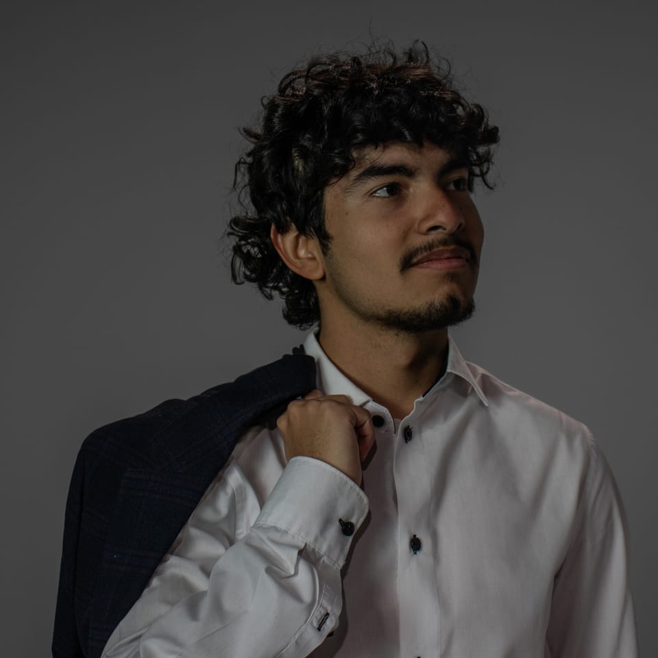 Young man with curly hair looking off to one side, a suit jacket slung over his shoulder.