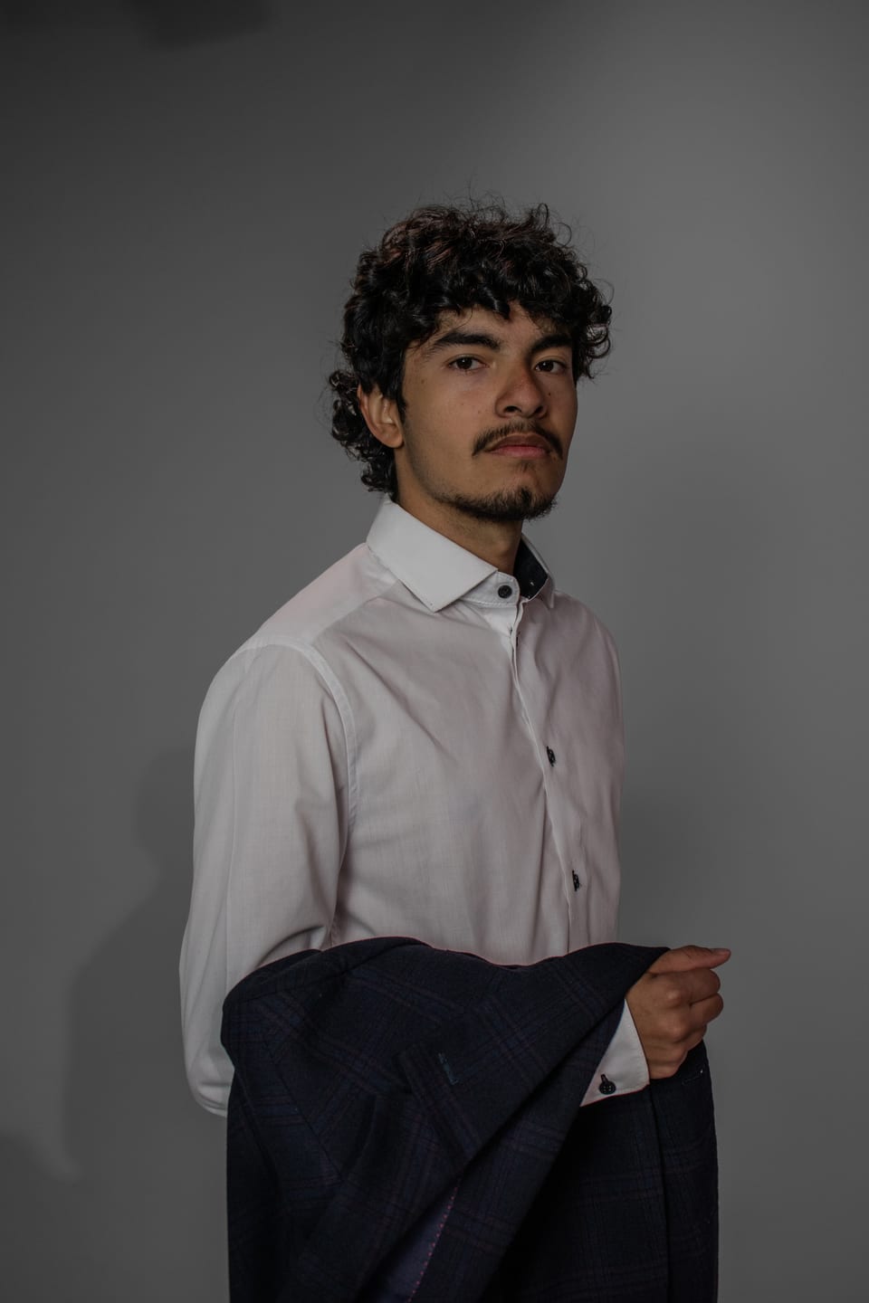 Young man in a white shirt holding his blazer at his side, glancing back at the camera.