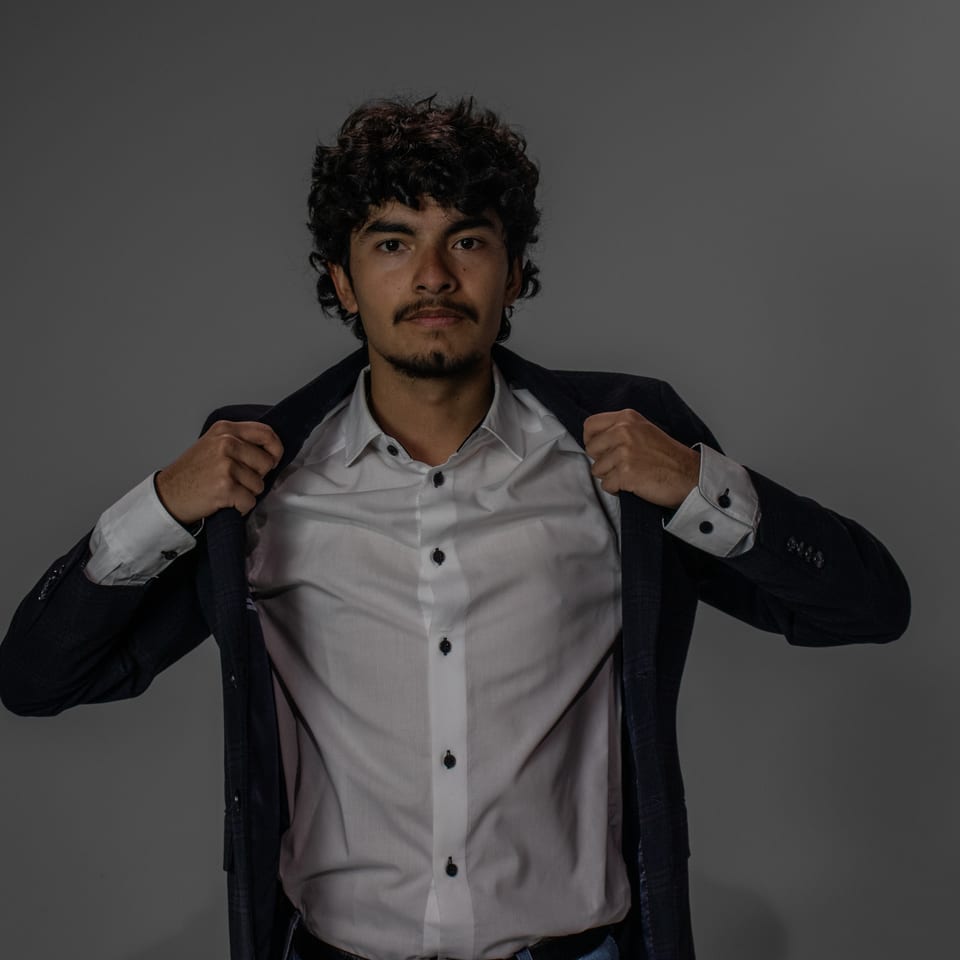 Young man pulling his blazer open with both hands over a white shirt.