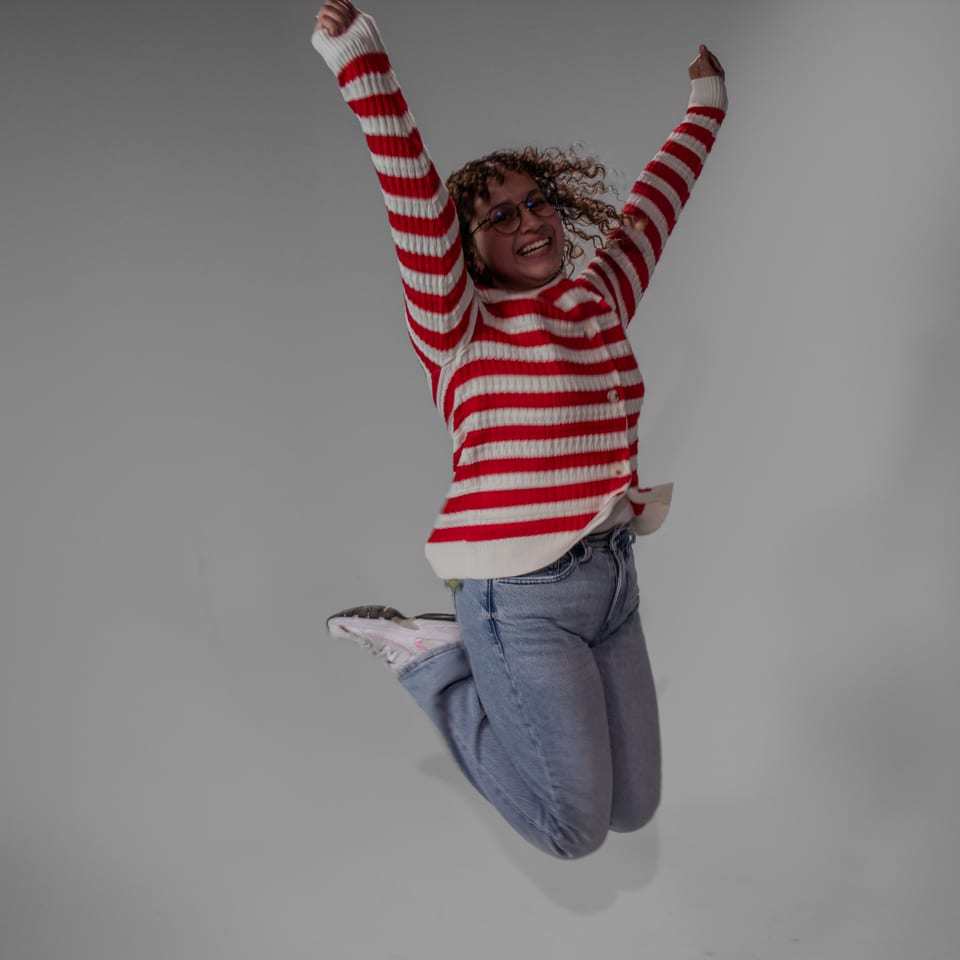 Woman in a striped sweater caught mid-jump with both arms raised.