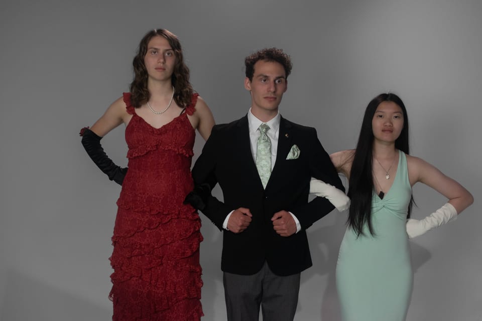 Three friends in formalwear side by side, hands on hips: a red gown, a dark suit and a mint gown.