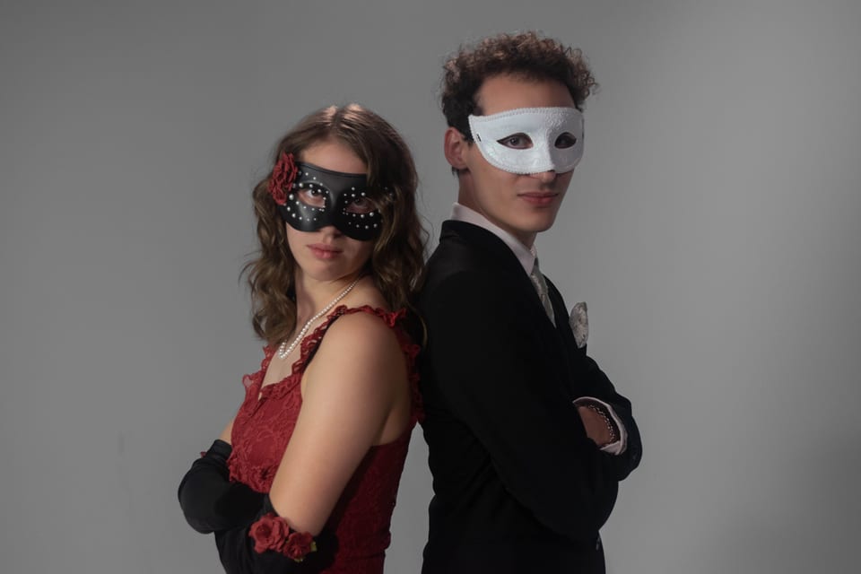 Two people in masquerade masks standing back to back with their arms crossed.