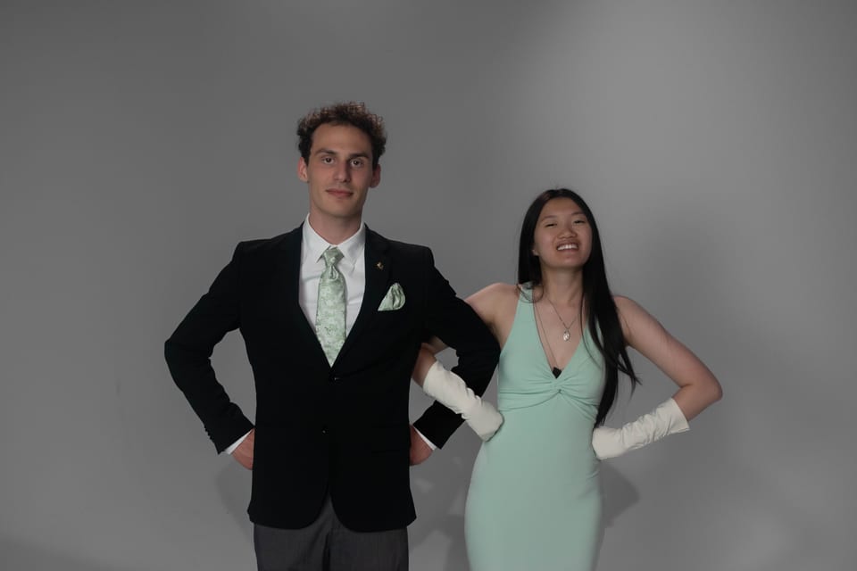 A couple standing with hands on hips, him in a dark suit and green tie, her in a mint gown and white gloves.