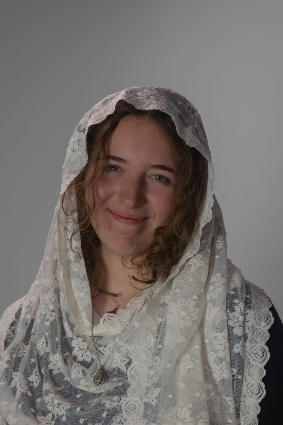 Woman in a white lace veil smiling softly at the camera.