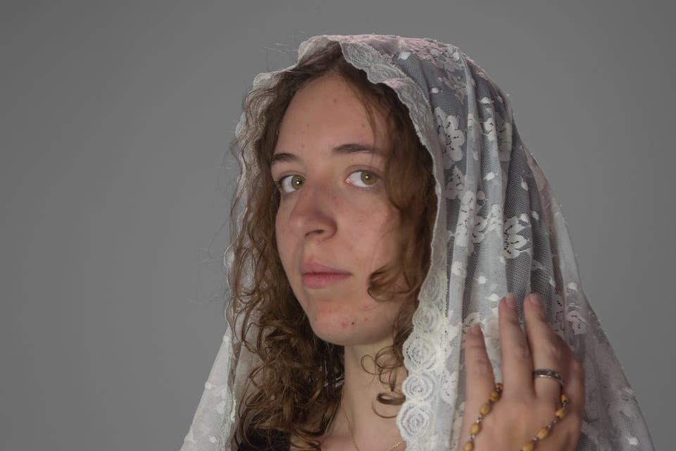 Woman in a lace veil looking straight into the camera, a rosary wrapped around her hand.