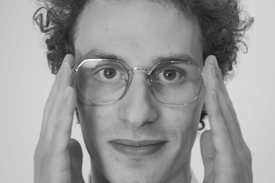 Black-and-white close-up of a young man framing his glasses with both hands.