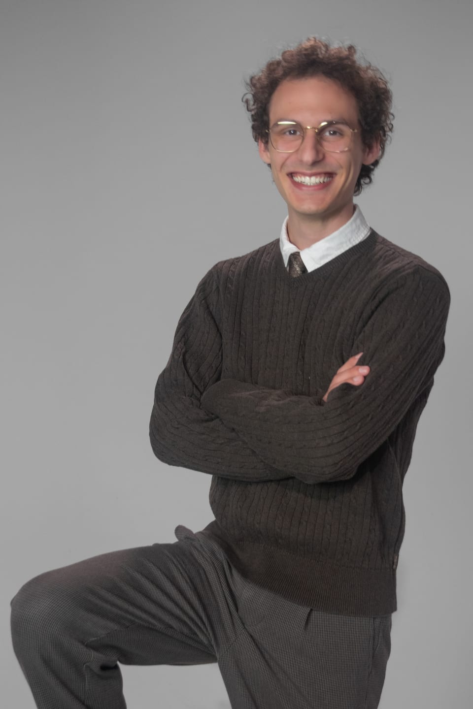 Grinning young man in glasses kneeling on one knee with his arms crossed.
