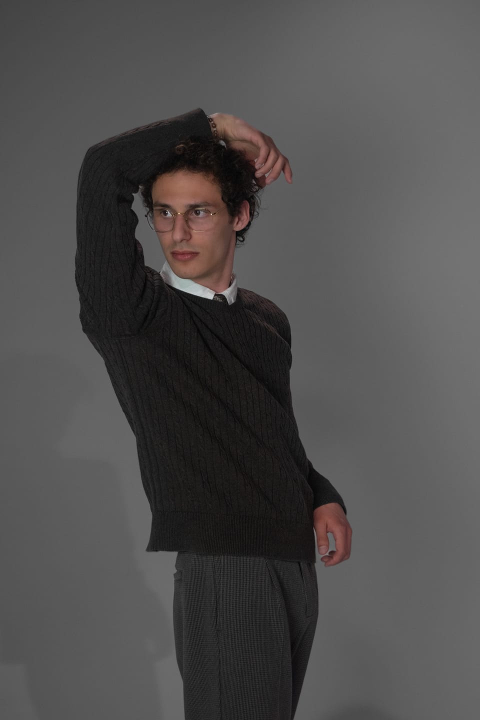 Young man in a dark sweater striking a dramatic pose, one arm bent over his head.
