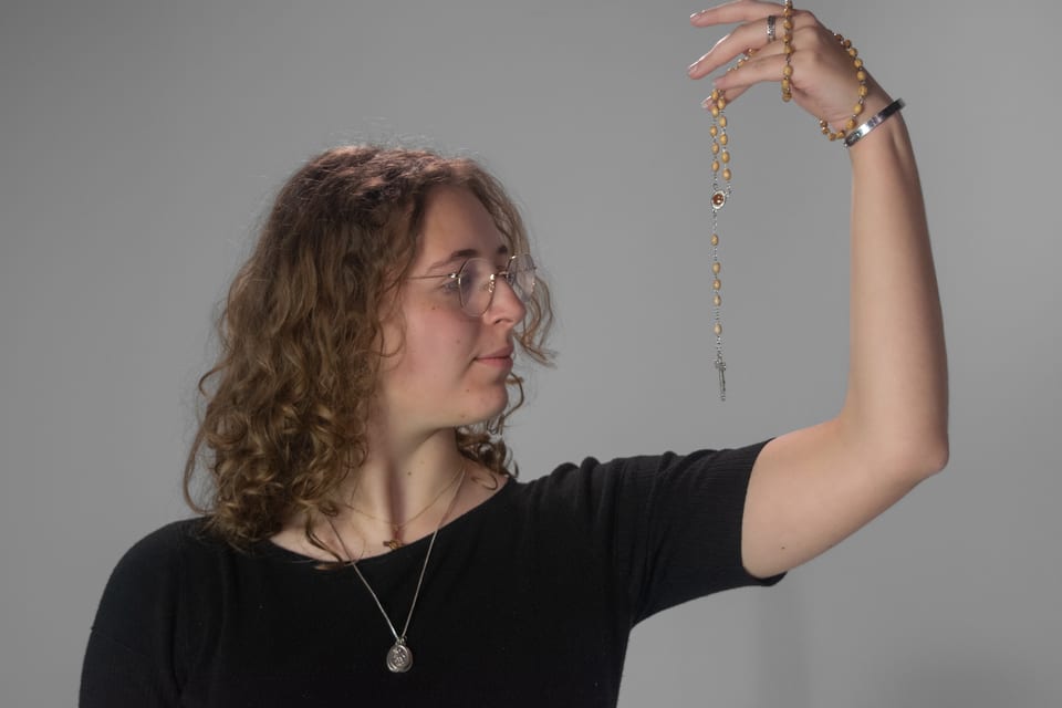 Woman in profile holding a rosary up at arm's length, looking at it.