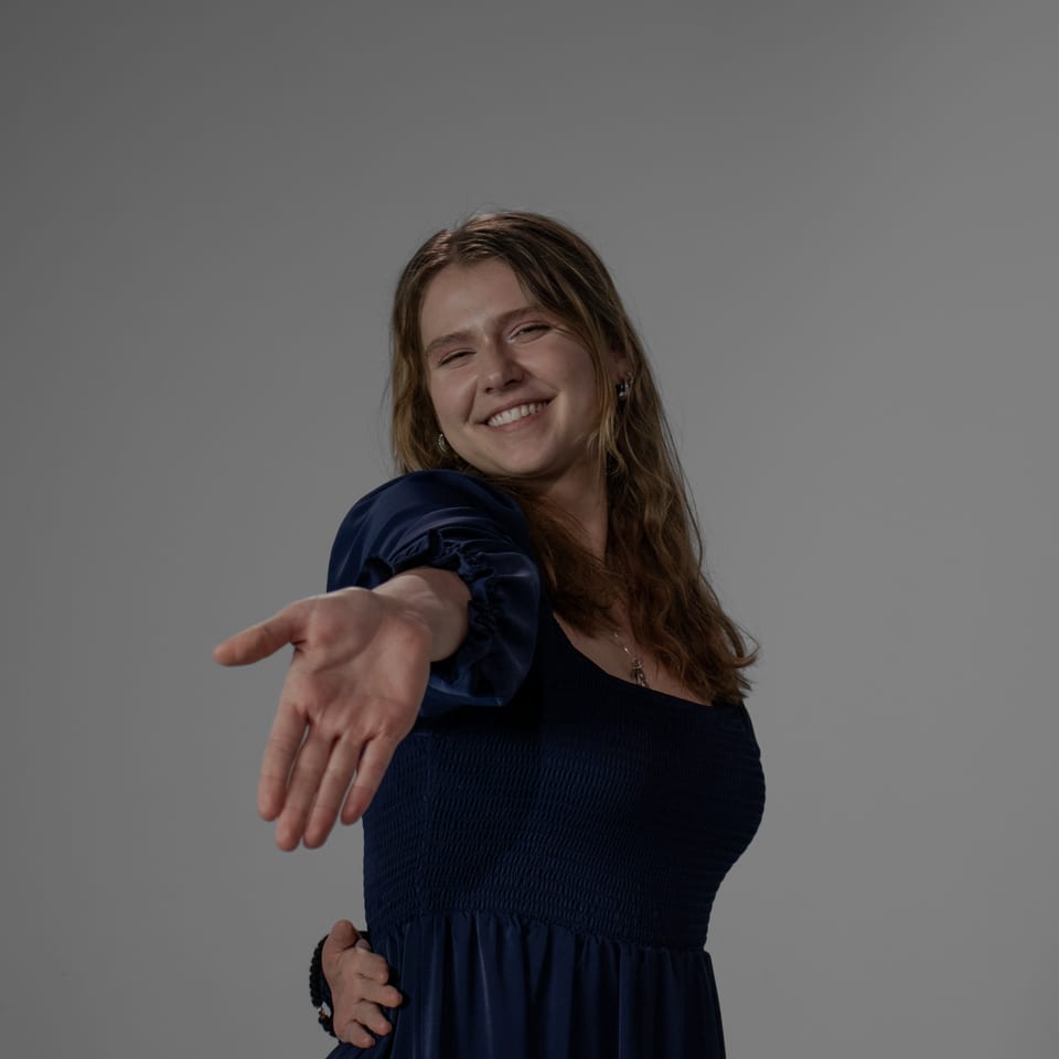 Laughing woman in a navy dress reaching one hand toward the camera.