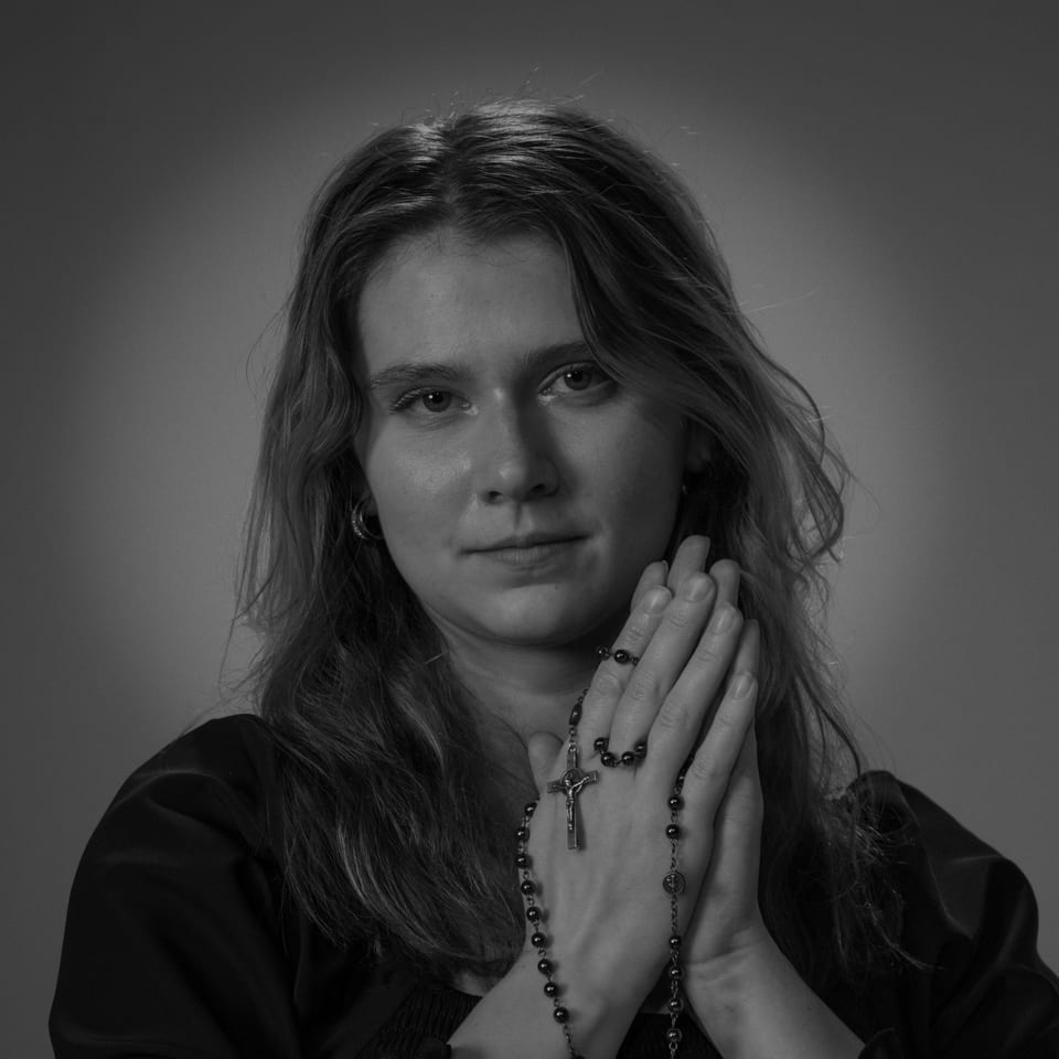 Black-and-white portrait of a woman with a rosary wound through her folded hands.