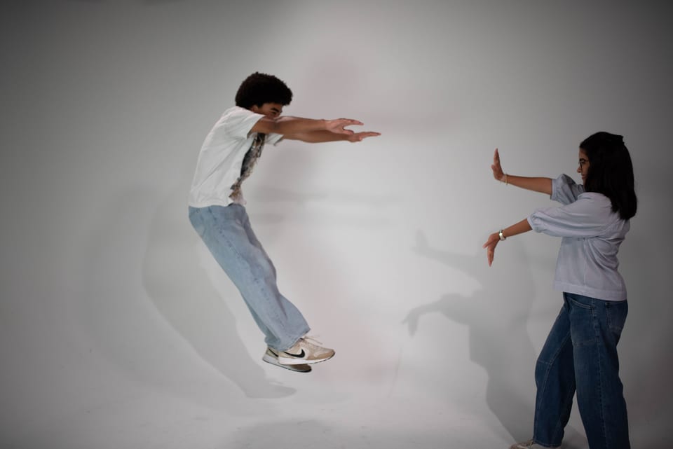A mock standoff: one young man leaps forward with arms outstretched while a young woman holds up a hand to stop him.