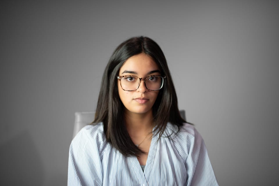 Young woman in glasses and a striped blouse seated in a chair, looking calmly at the camera.