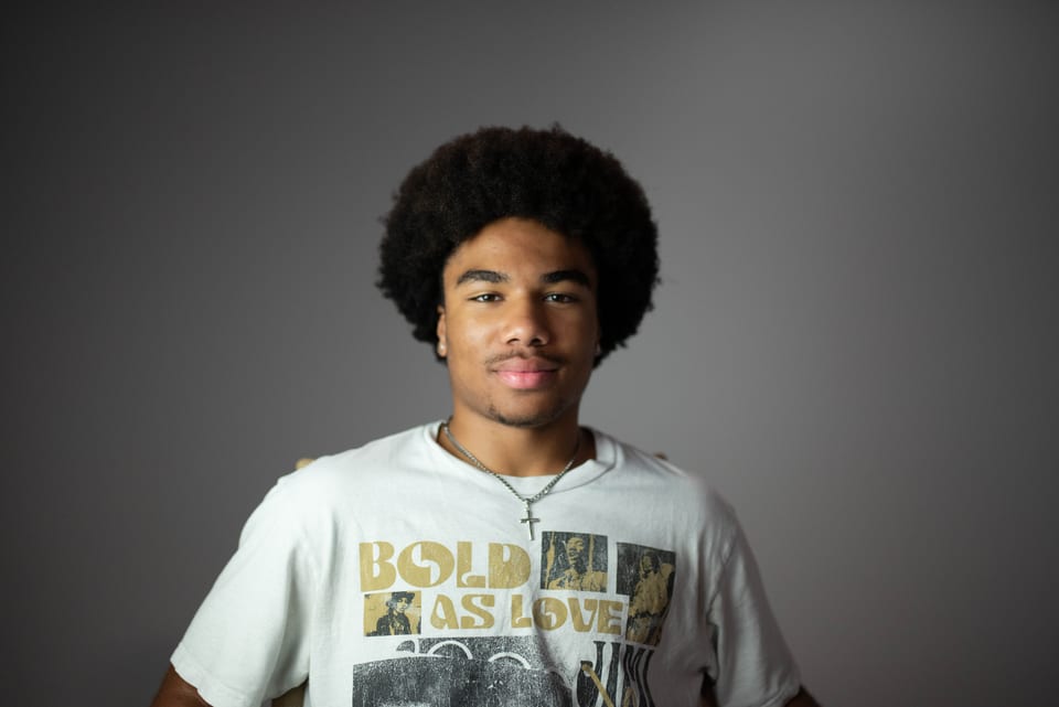 Young man with an afro in a Jimi Hendrix T-shirt, looking straight into the camera.