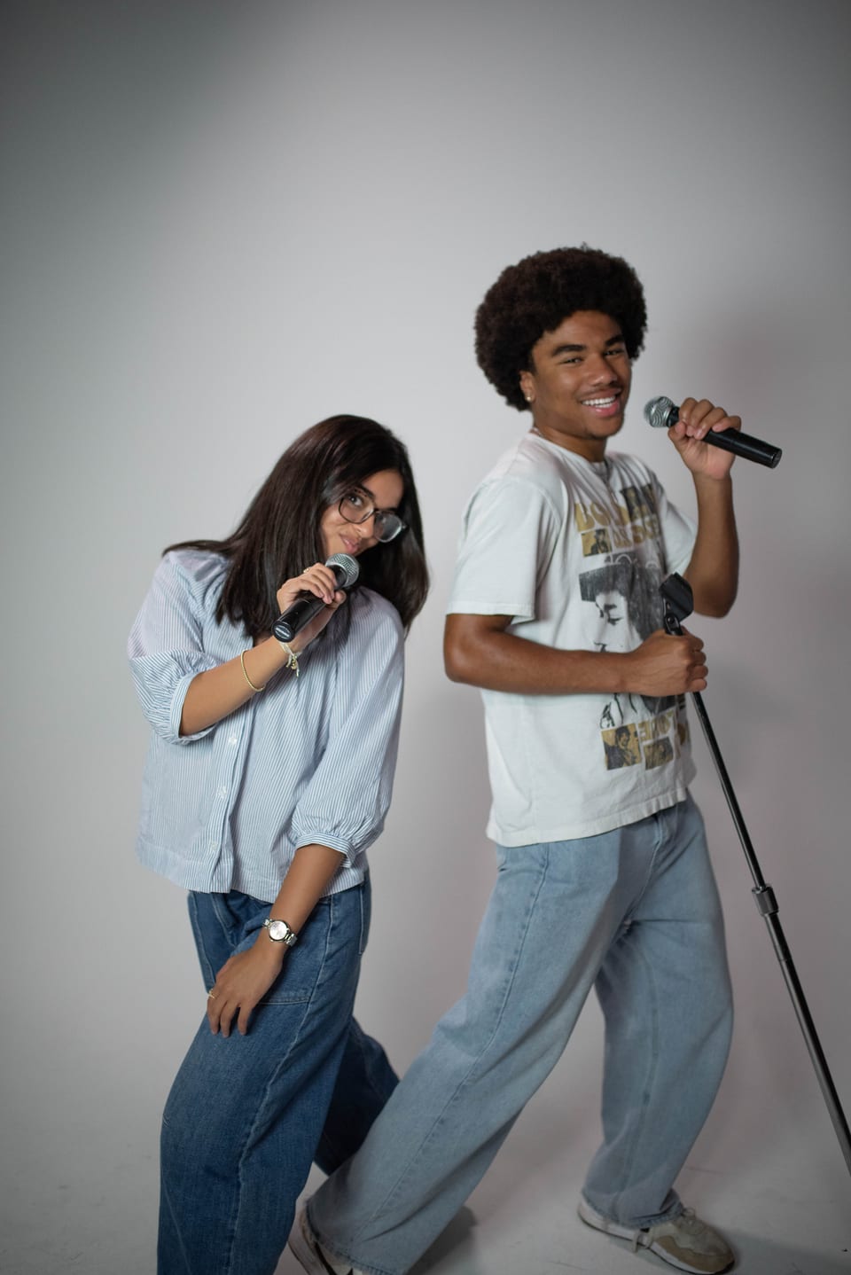 Two friends hamming it up with microphones, one leaning on a mic stand mid-song.