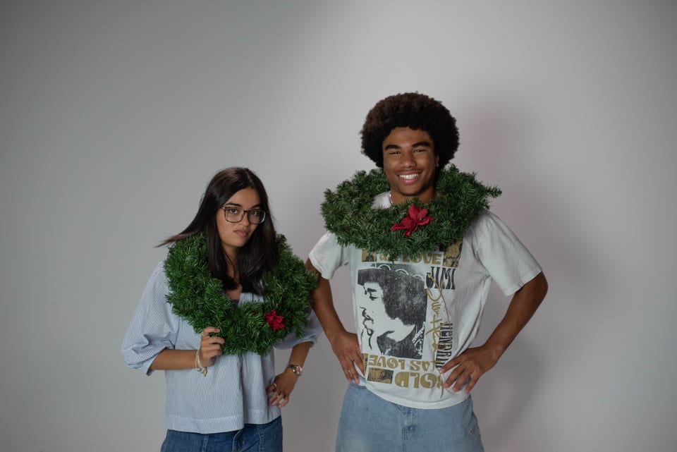 Two coworkers posing with Christmas wreaths draped around their necks, hands on hips.