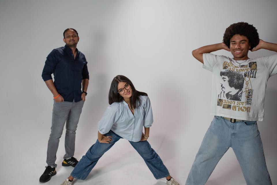 Three coworkers posing in a row: one standing tall, one in a wide stance, one with his hands behind his head.