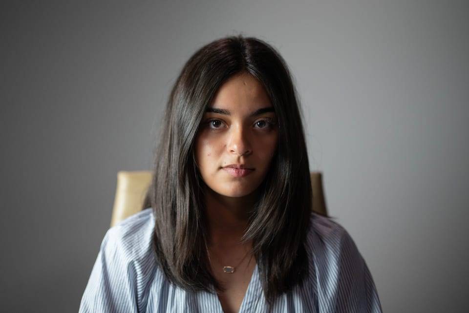 Young woman with straight dark hair seated in a chair, looking directly at the camera.